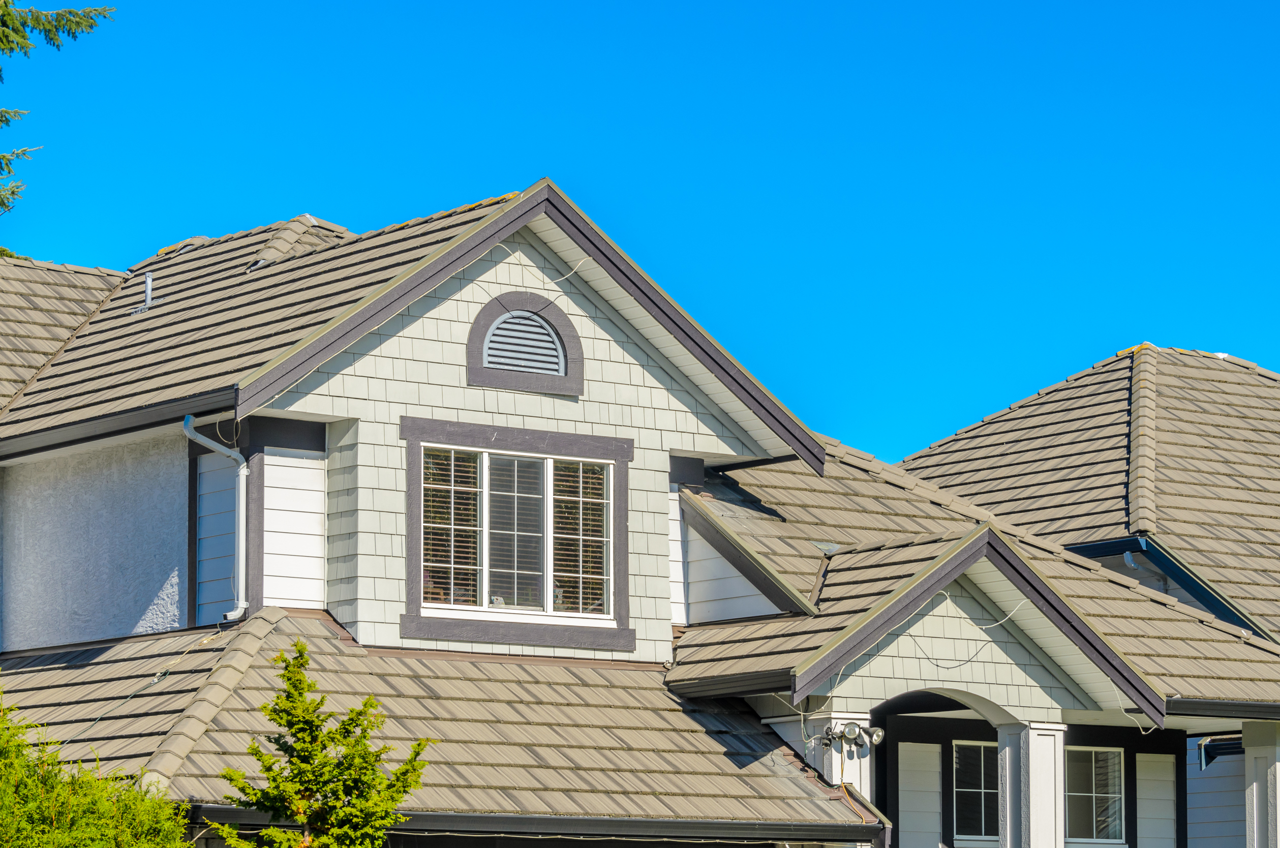 A dark brown roof on a mosaic-styles brown brick house with greenery around it